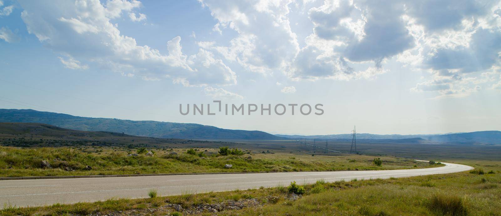 Evening summer landscape with green grass, road and clouds