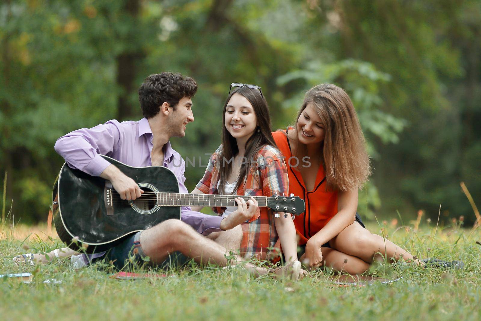 group of students with a guitar relax sitting on the grass in the city Park.