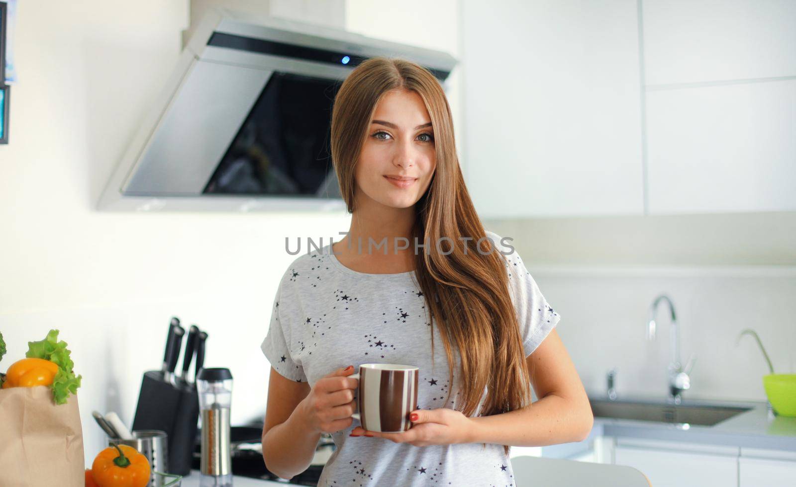 Young woman holding grocery shopping bag with vegetables standing in the kitchen