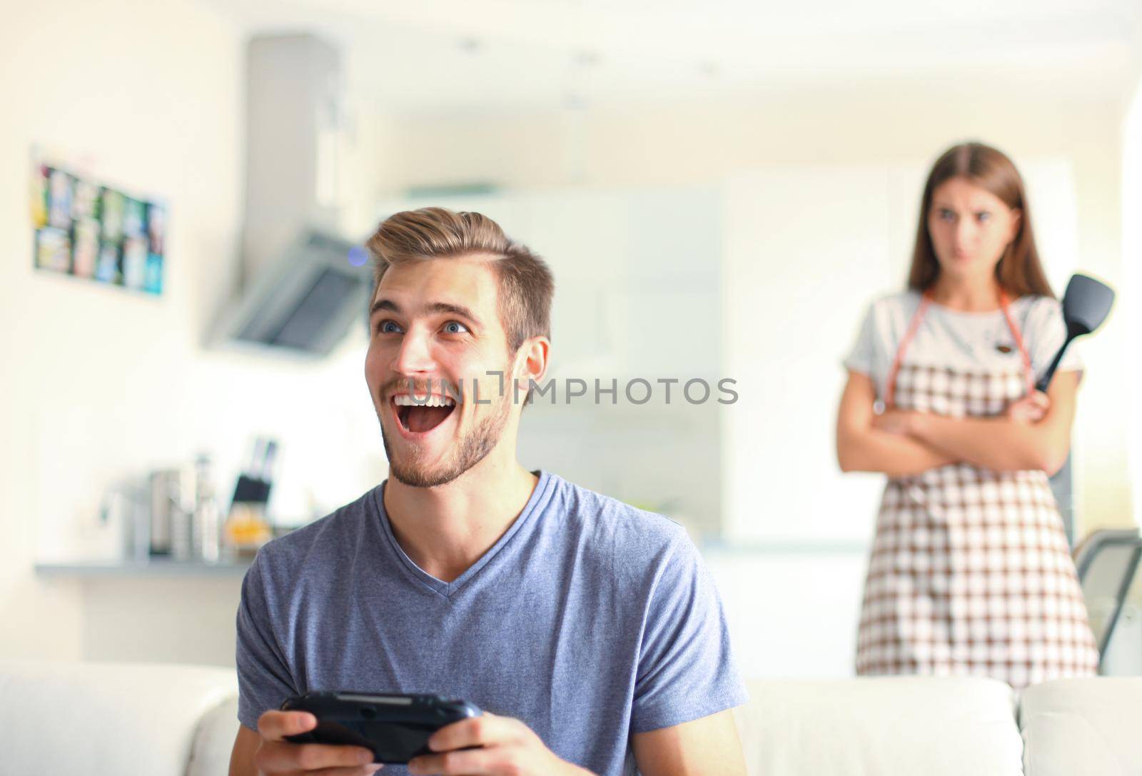 Man playing video games while his girlfriend cooking in the kitchen