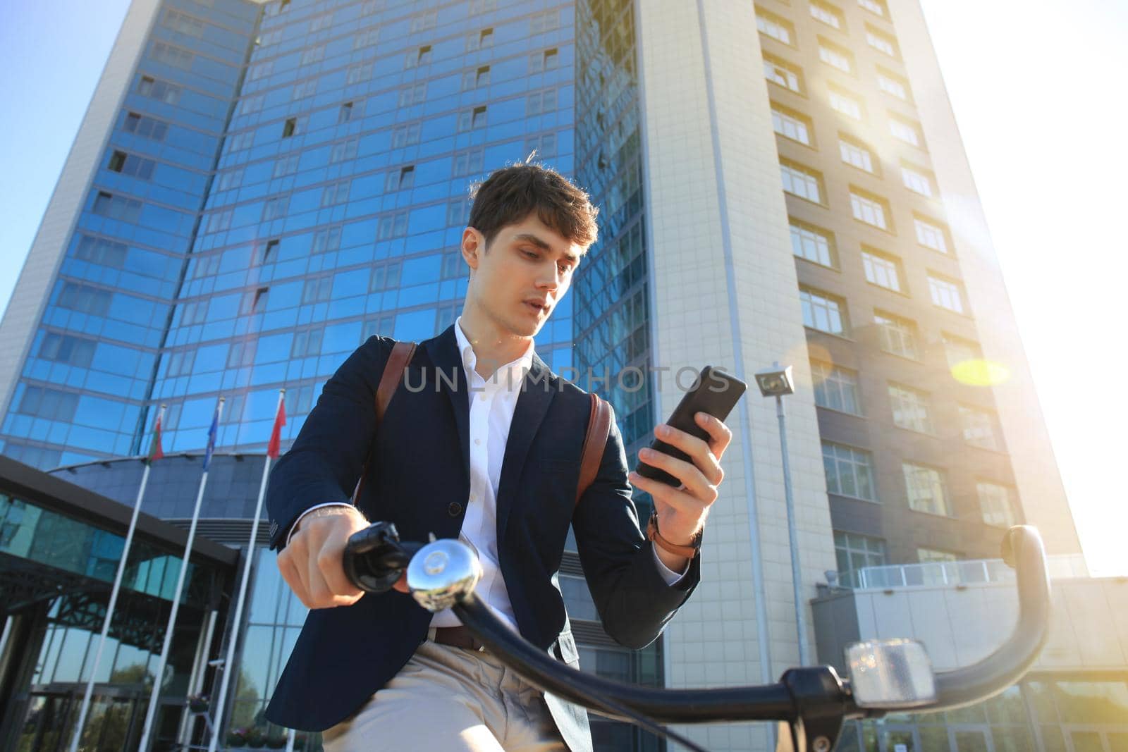 Young businessman with bicycle and smartphone on city street.