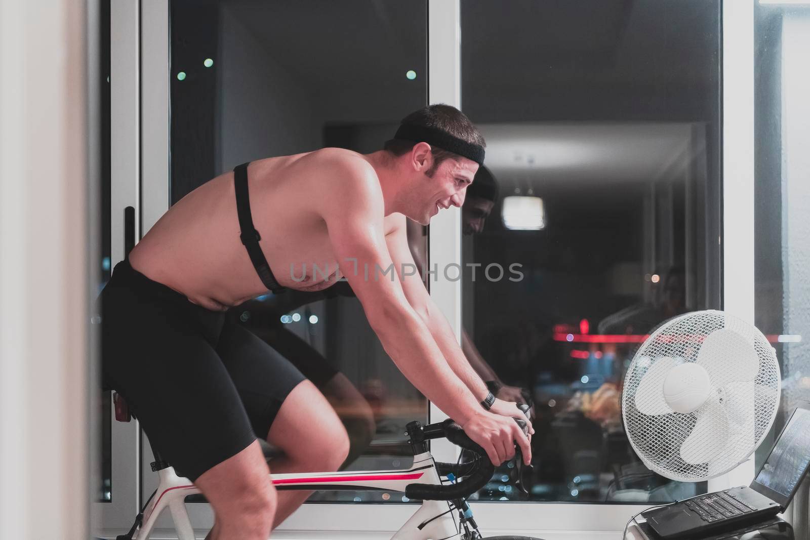 Man cycling on the machine trainer he is exercising in the home at night playing online bike racing game by dotshock