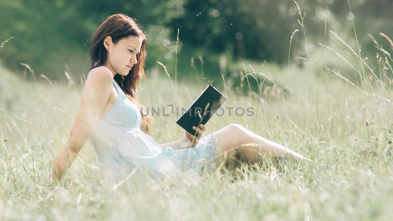 girl student reading a book sitting on the lawn on a summer day . photo with copy space