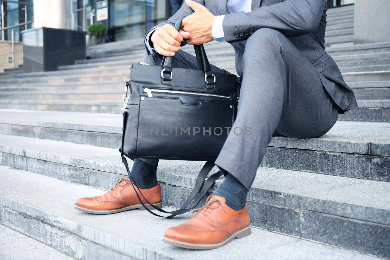 Handsome male business executive sitting on stairs outside a building. by tsyhun