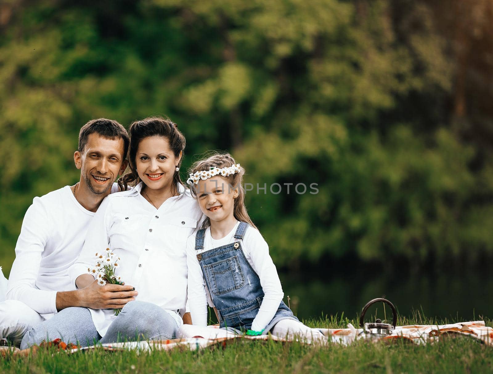 pregnant mother and happy father and little daughter at a picnic in the Park on a Sunny day. the photo has a empty space for your text