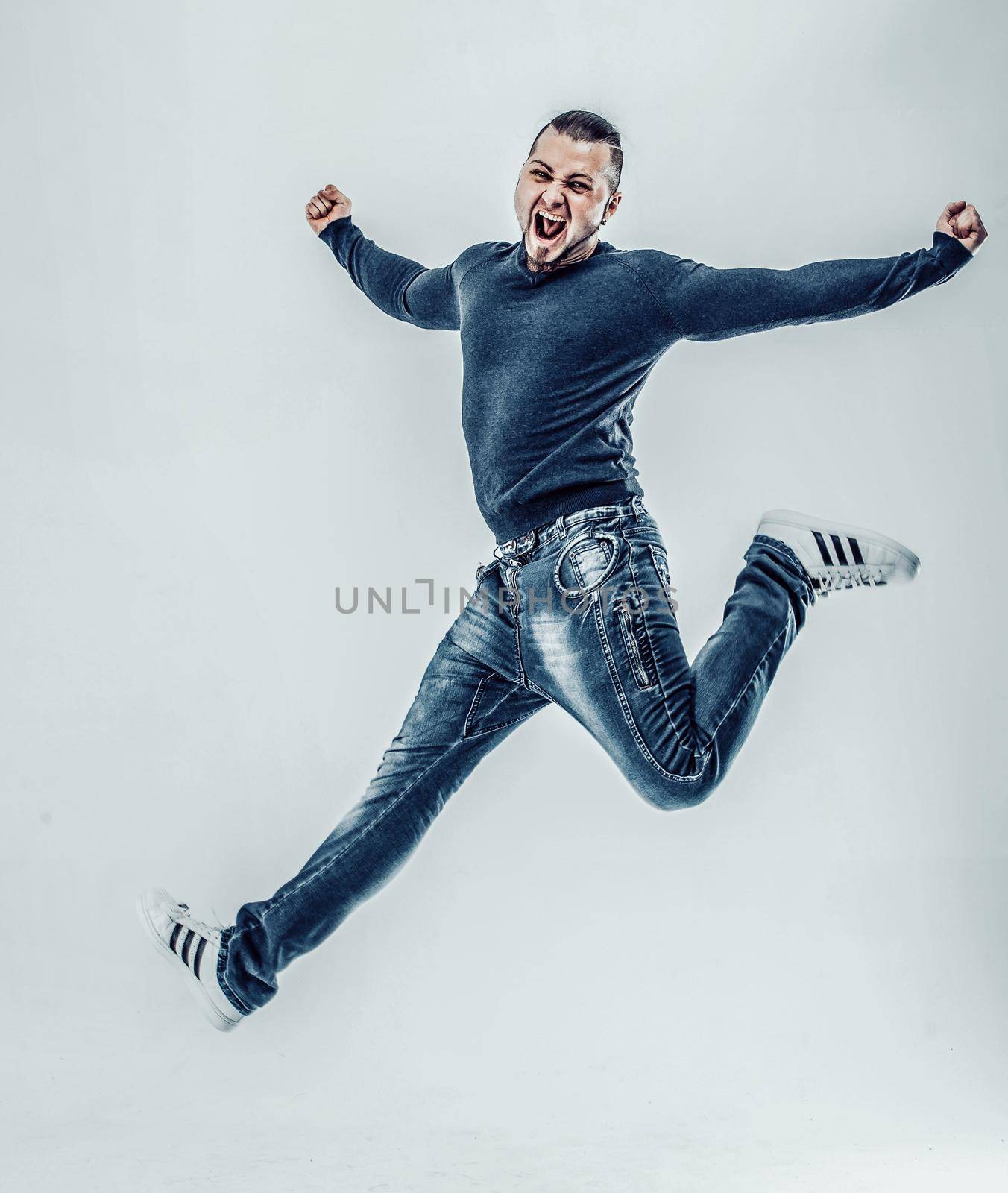 A young boy jumps for joy and happiness and raises her arms up on white background