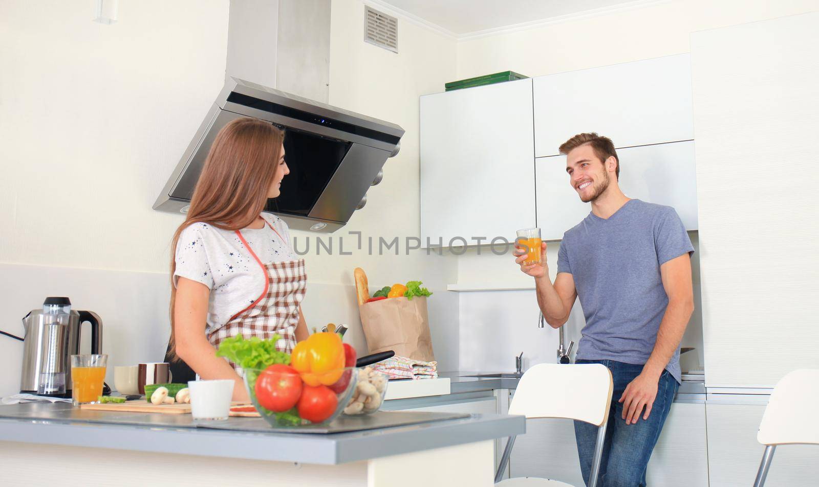 Beautiful young couple in pajamas is looking at each other and smiling while cooking in kitchen at home.