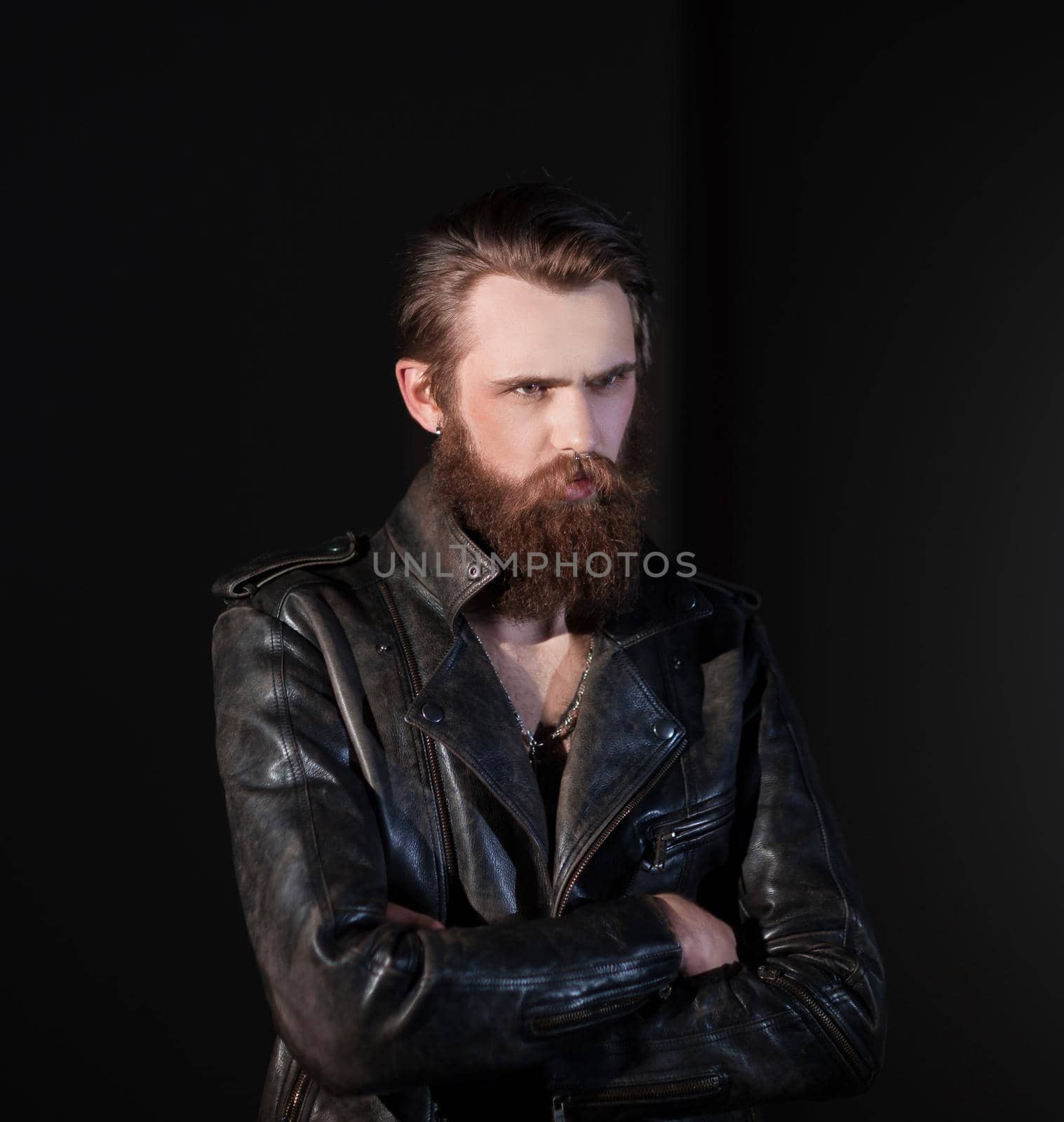 serious bearded man in a leather jacket looking somewhere to the side.isolated on black background