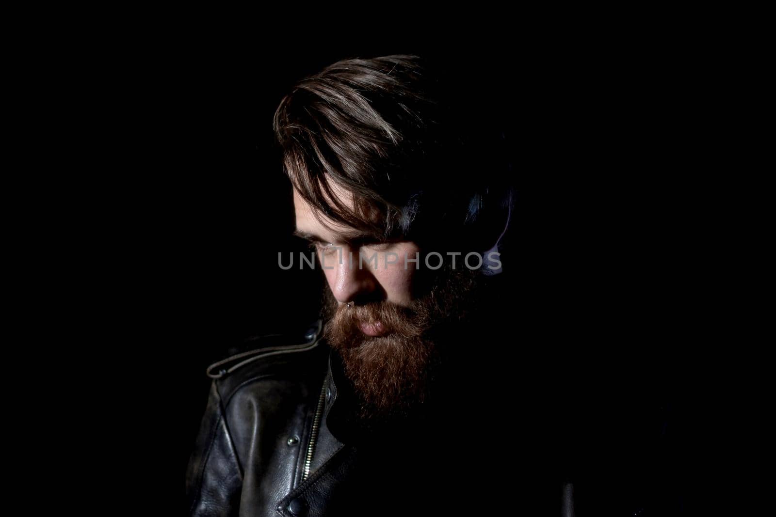 brooding bearded hipster in a leather jacket looking somewhere to the side. isolated on black background
