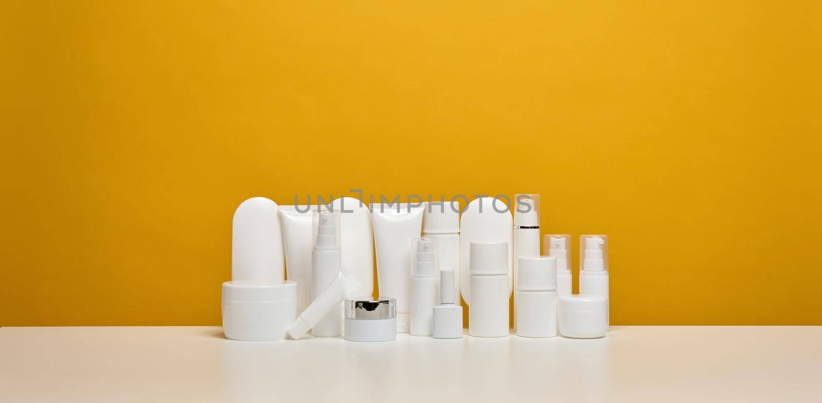 jar, bottle and empty white plastic tubes for cosmetics on a yellow background. Packaging for cream, gel, serum, advertising and product promotion by ndanko