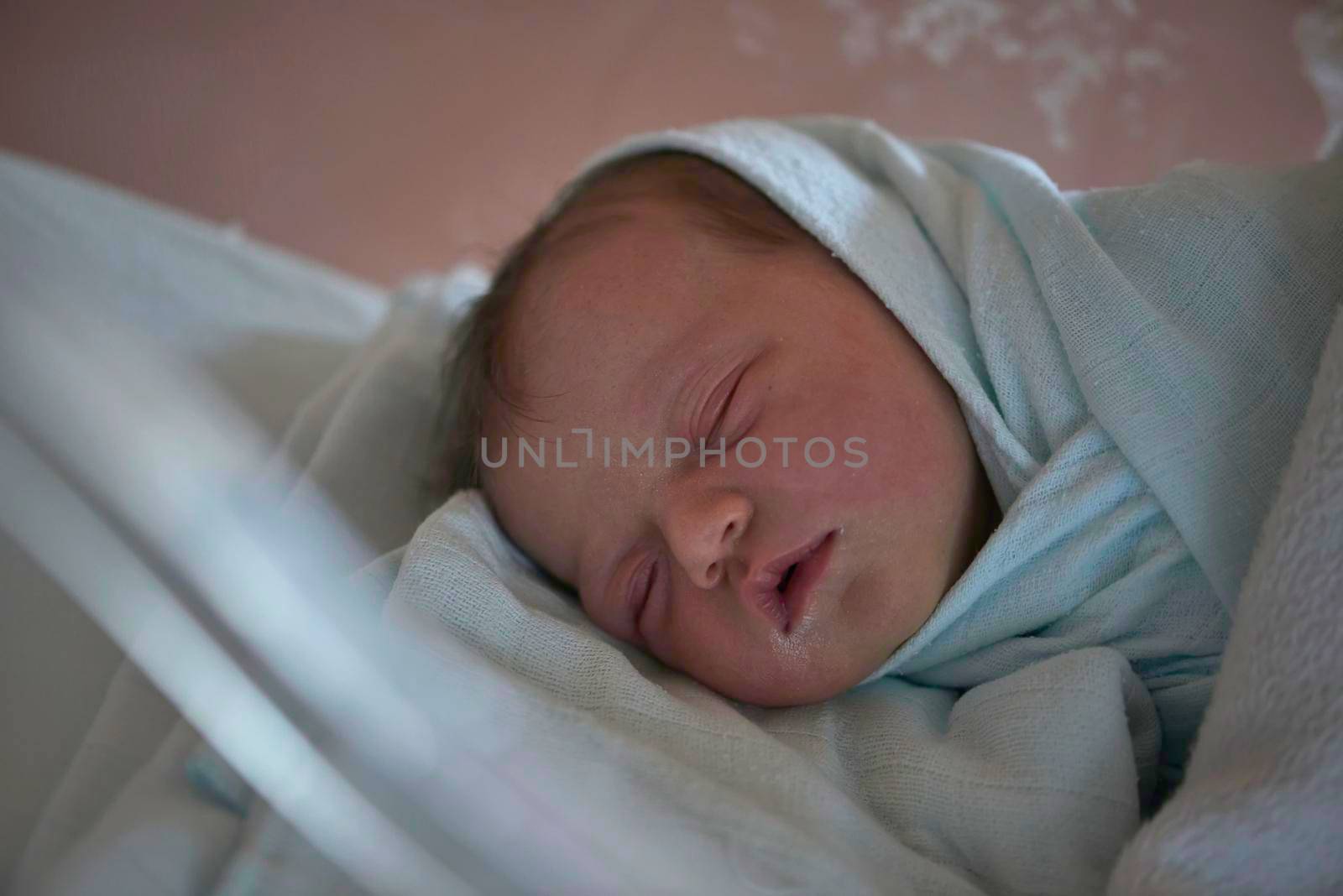newborn baby child sleeping in plastic bed at hospital  wearing blanket coat