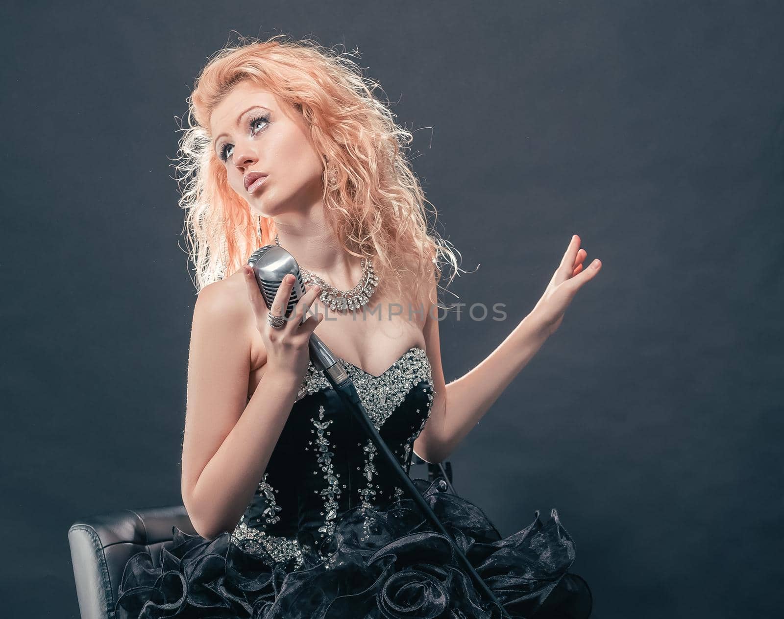 beautiful girl singer performing a song sitting on a chair.isolated on a dark background