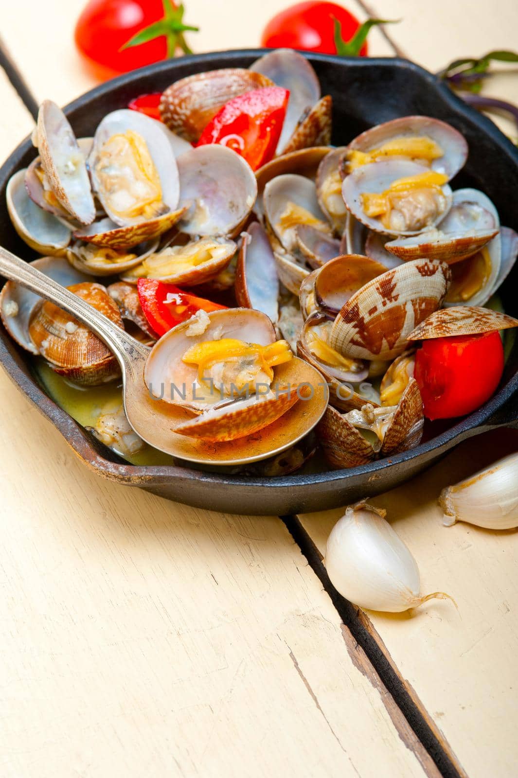 fresh clams stewed on an iron skillet over wite rustic wood table 