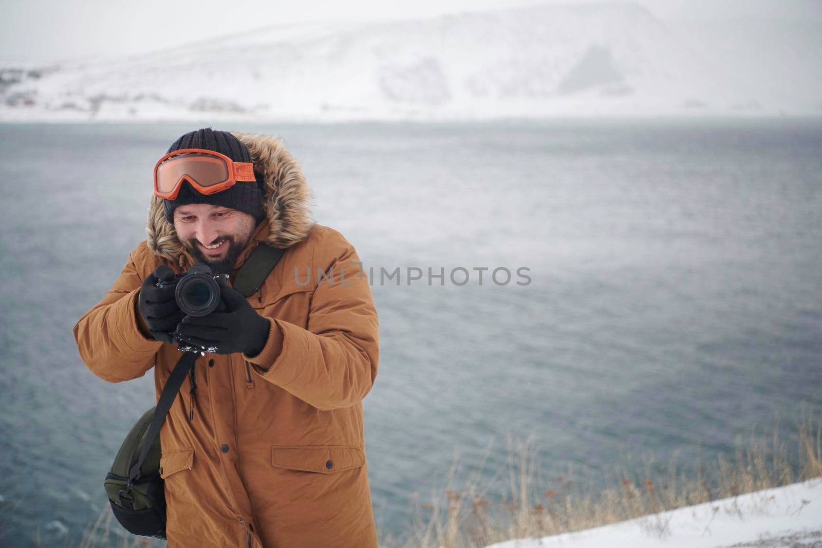 photographer tourist explorer at winter in stormy weather wearing warm  fur jacket and taking photos photos of nature and landscapes