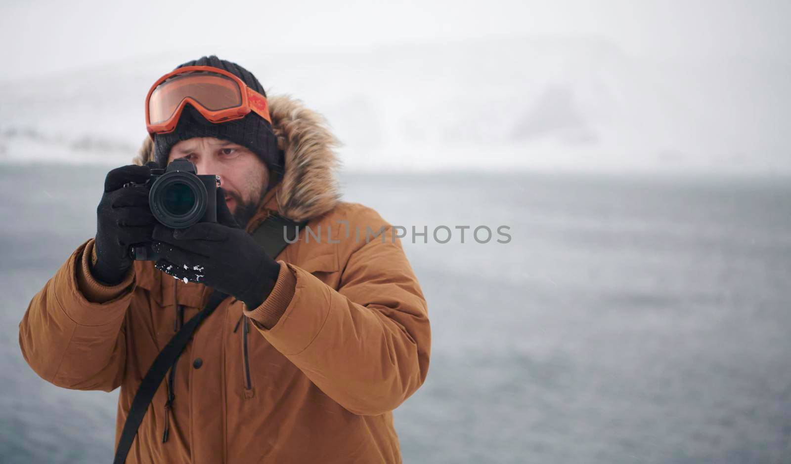 photographer tourist explorer at winter in stormy weather wearing warm  fur jacket and taking photos photos of nature and landscapes