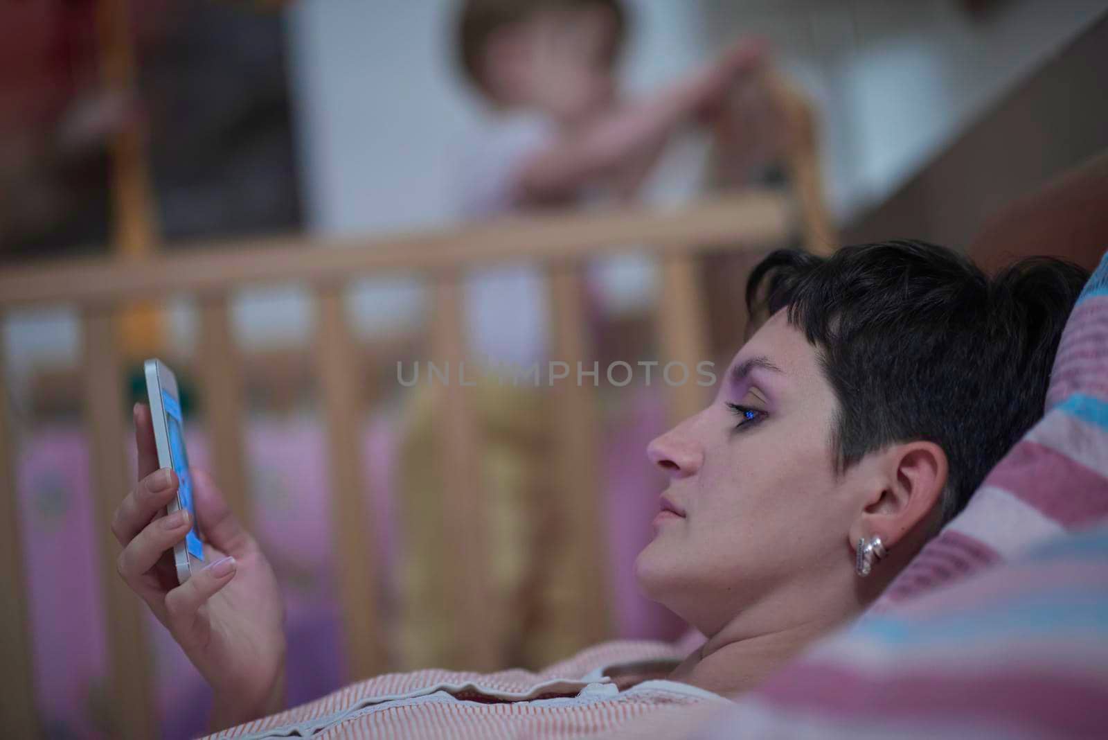 busines woman as mother is using smarphone in bed while baby sleeping in bed