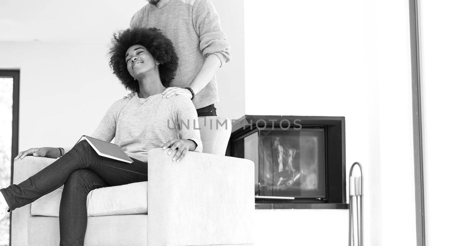 Young beautiful multiethnic couple hugging in front of fireplace at home when reading a book at autumn day