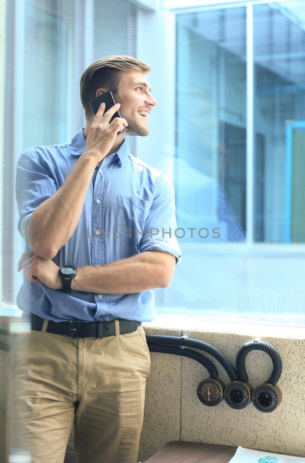 Smiling businessman standing and using mobile phone in office by tsyhun