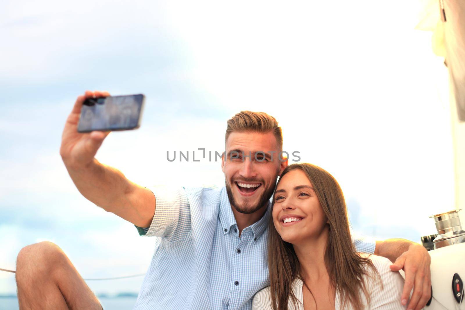 Happy couple taking a selfie after engagement proposal at sailing boat, relaxing on a yacht at the sea.