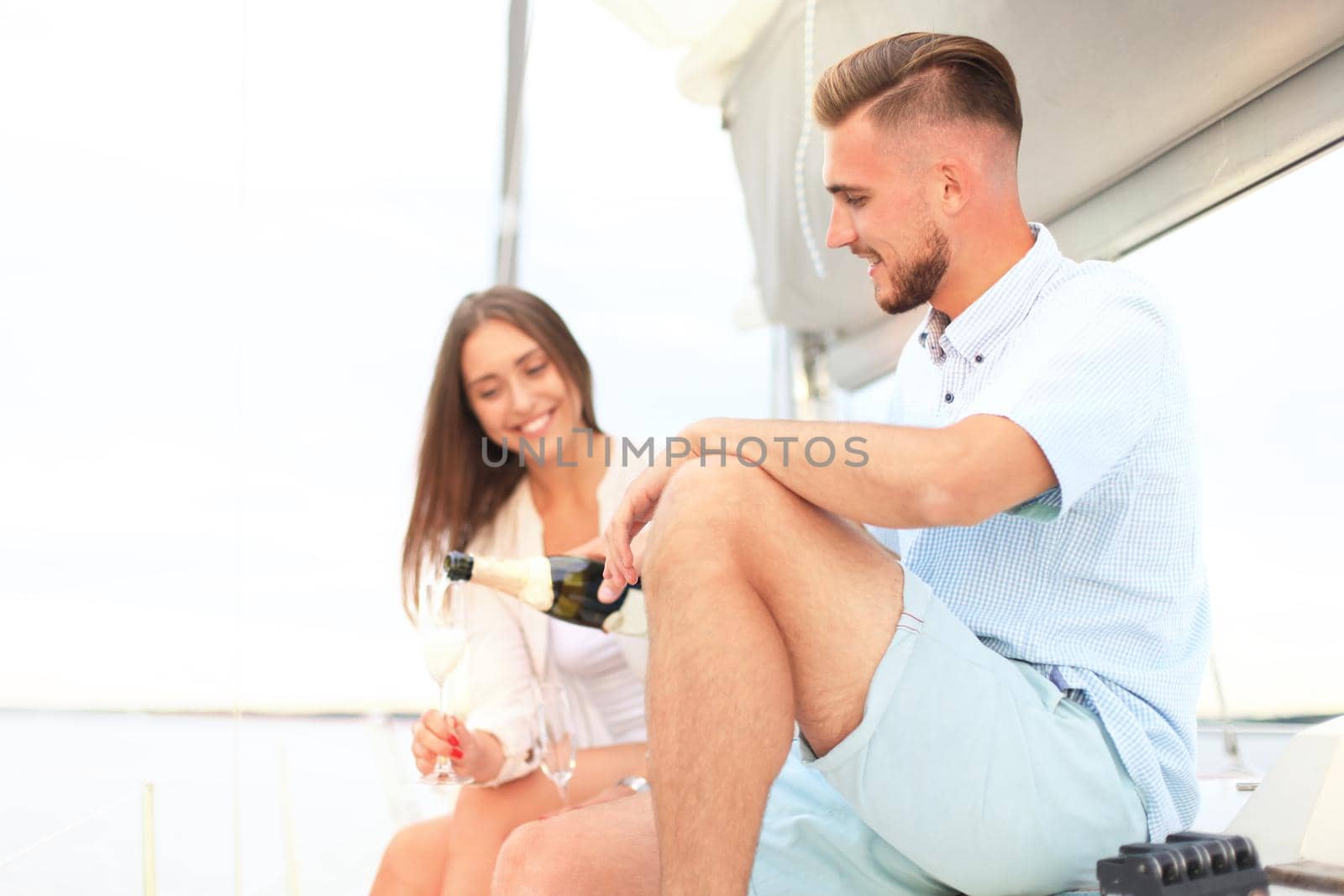 Smiling young couple with champagne and looking at each other while sitting on the board of yacht.