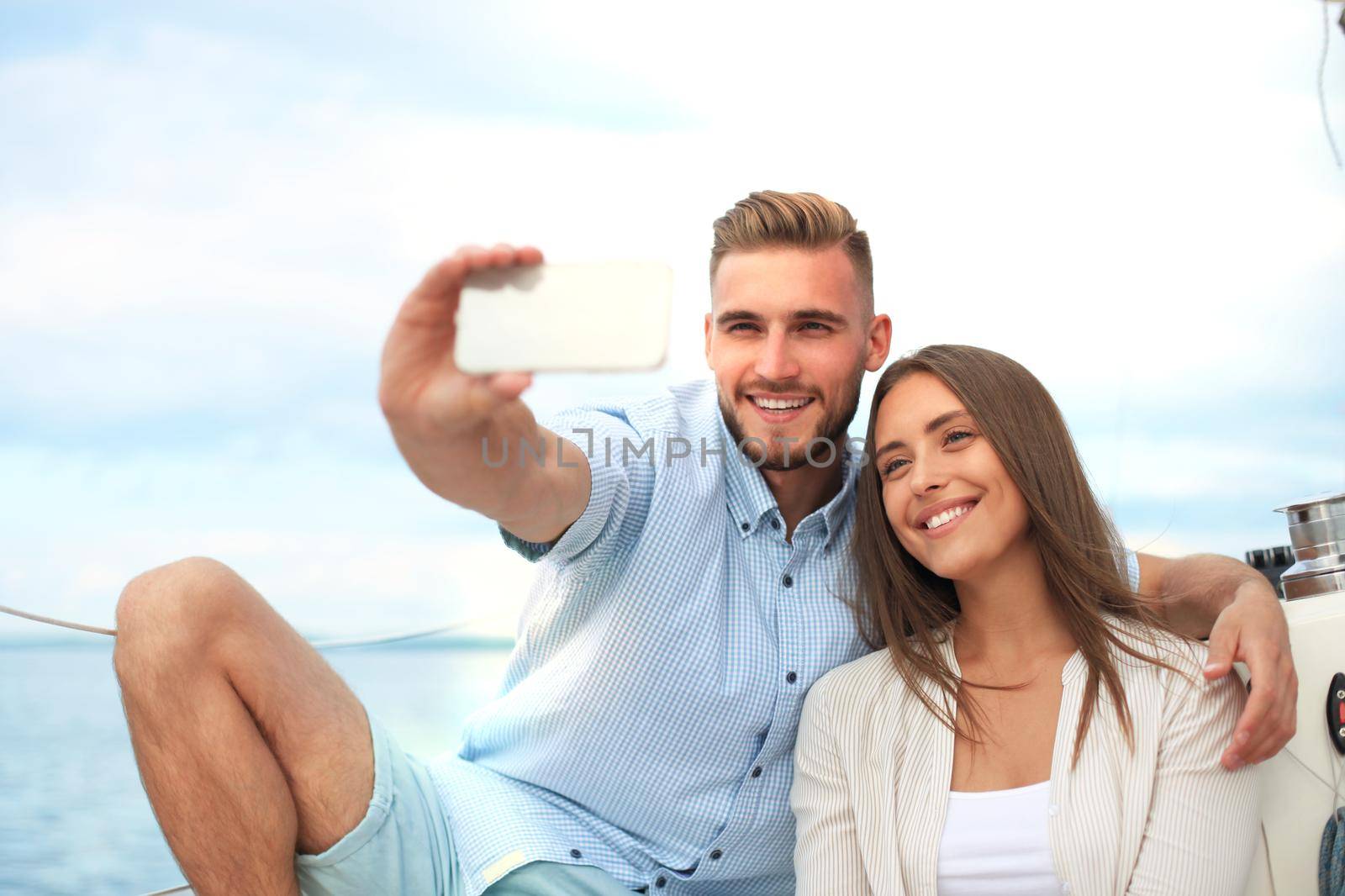 Happy couple taking a selfie after engagement proposal at sailing boat, relaxing on a yacht at the sea.