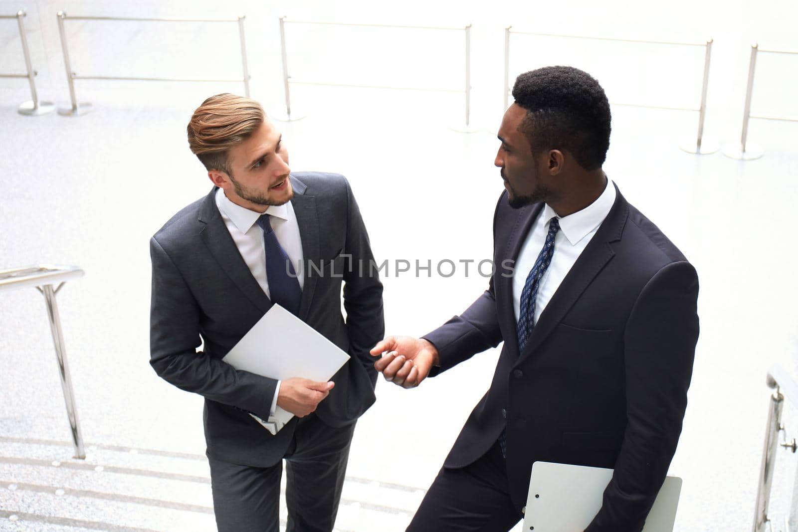Two multinational young businessmen talking while stairs in modern office building.