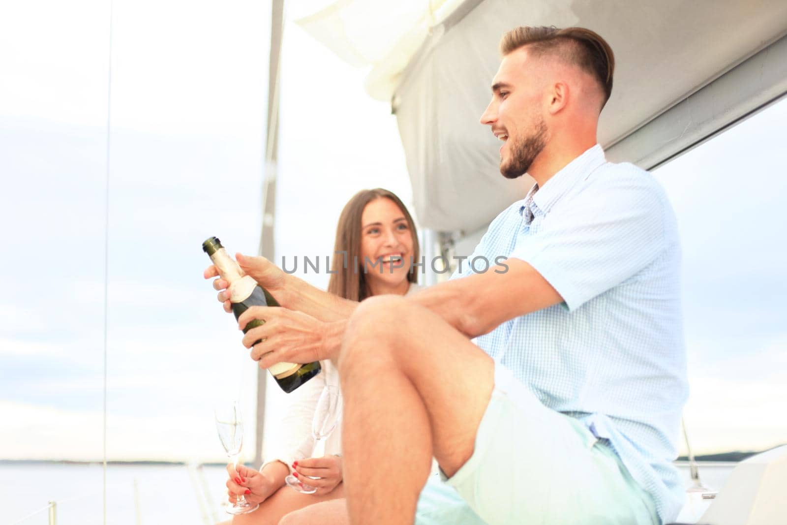 Smiling young couple with champagne and looking at each other while sitting on the board of yacht.