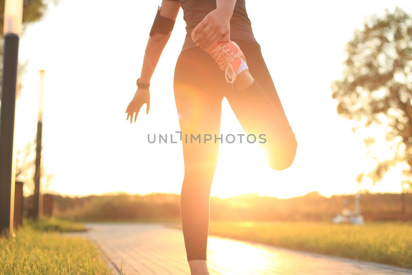 Young attractive sporty fitness woman runner warming up before run at sunset or sunrise on city
