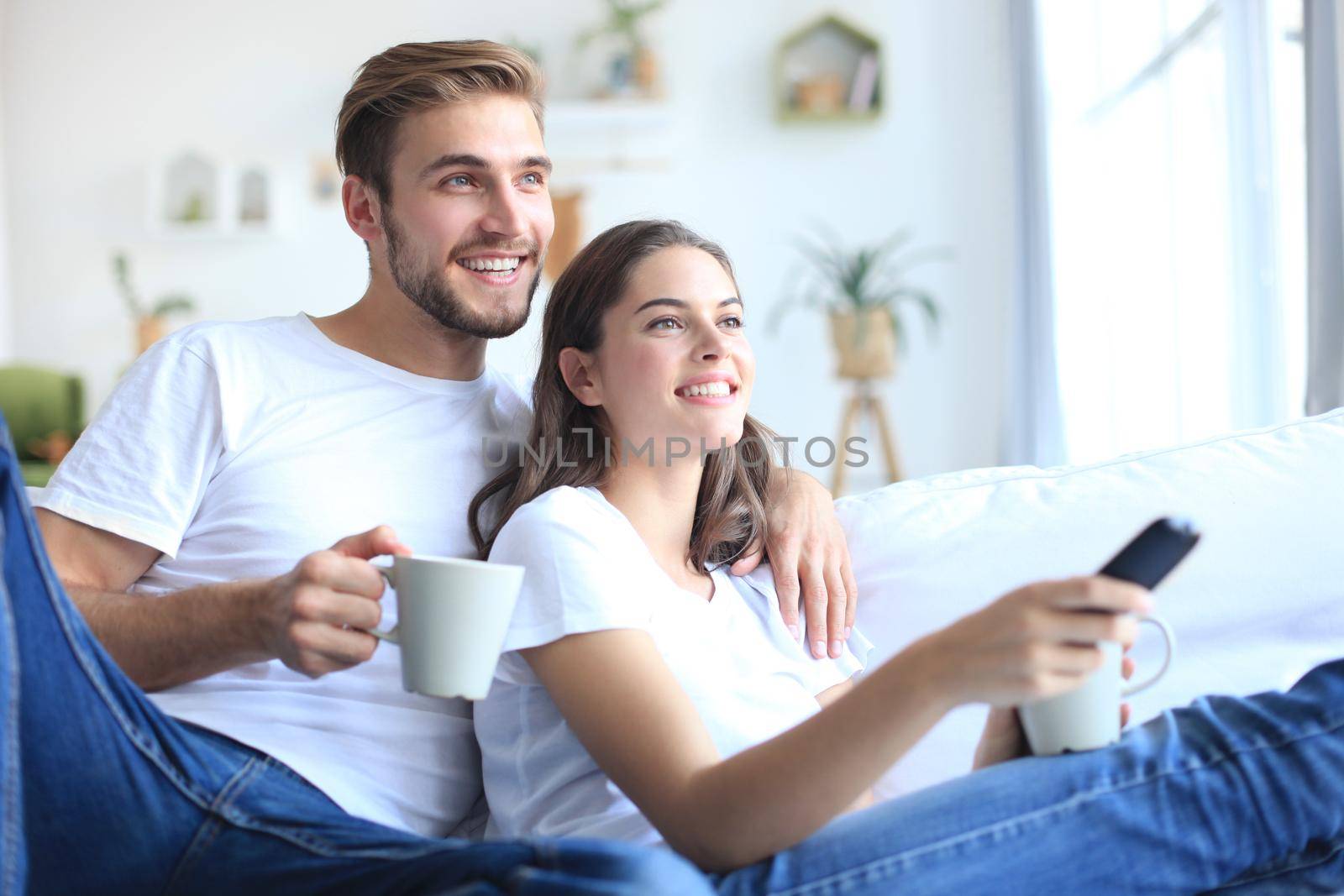 Young loving couple on sofa at home watching tv and laughing. by tsyhun