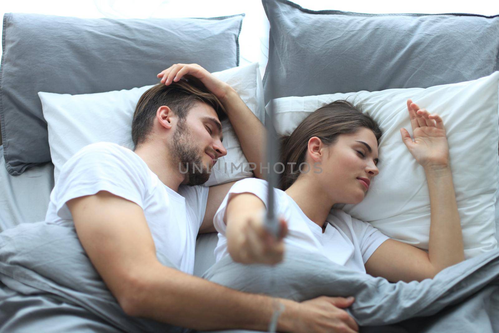 Beautiful young loving couple sleep and making selfie with stick in the bed. by tsyhun