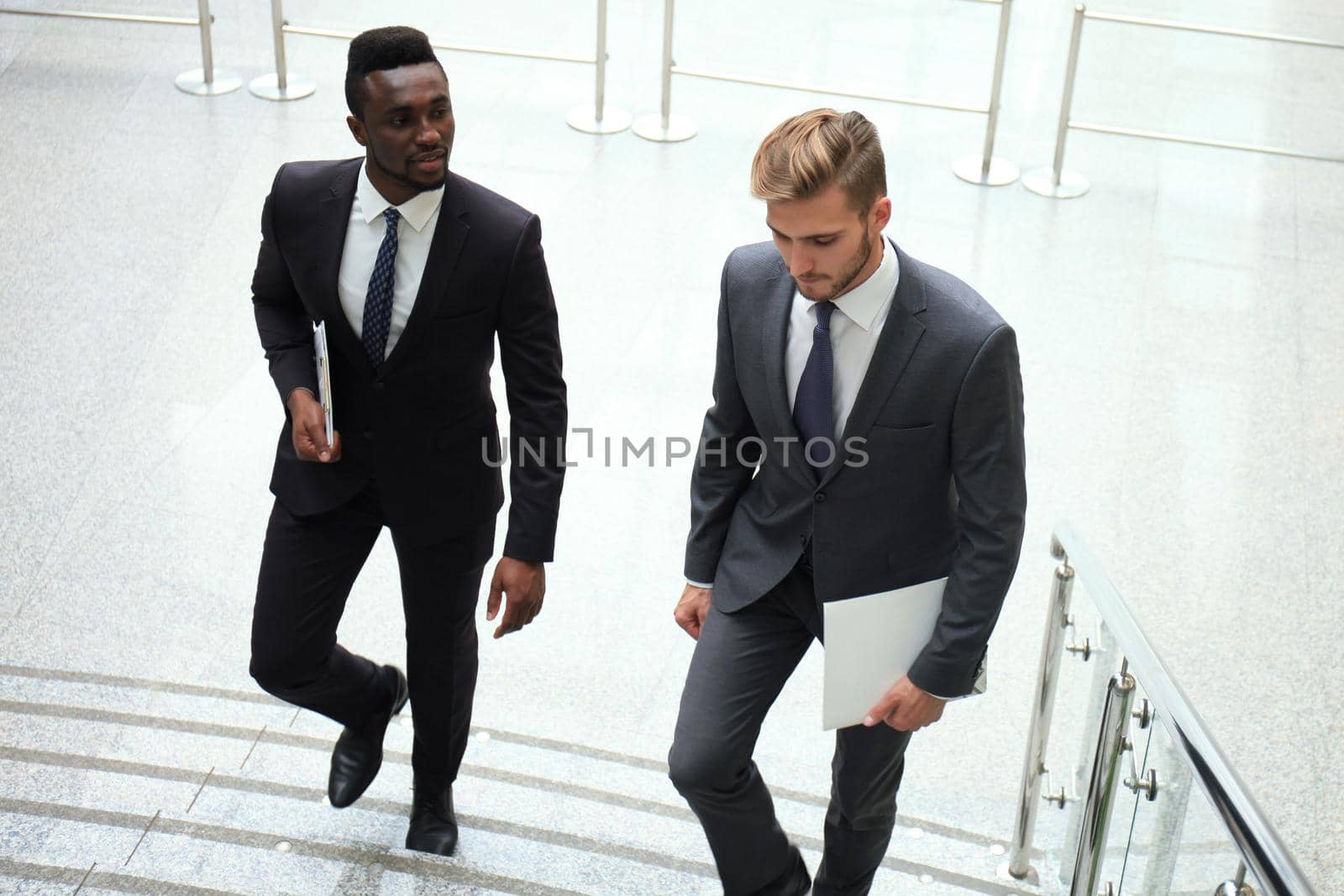 Two multinational young businessmen talking while stairs in modern office building. by tsyhun