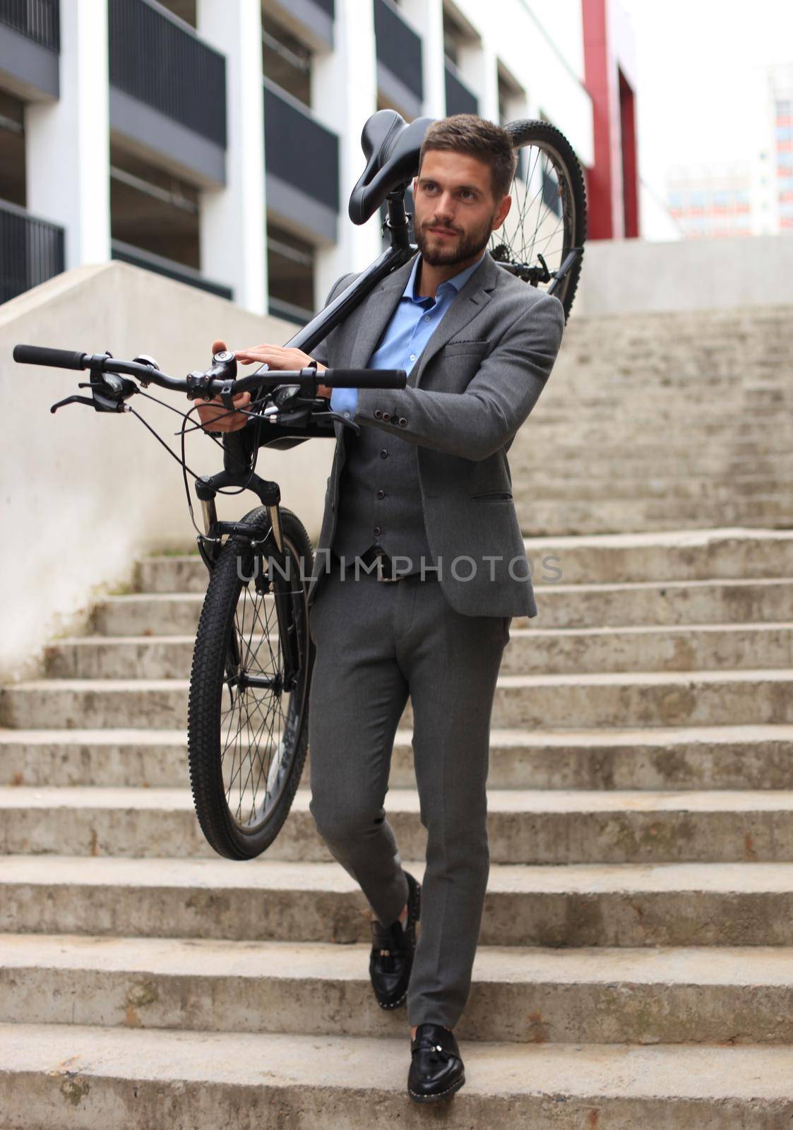 Confident young businessman carrying his bicycle while walking outdoors. by tsyhun