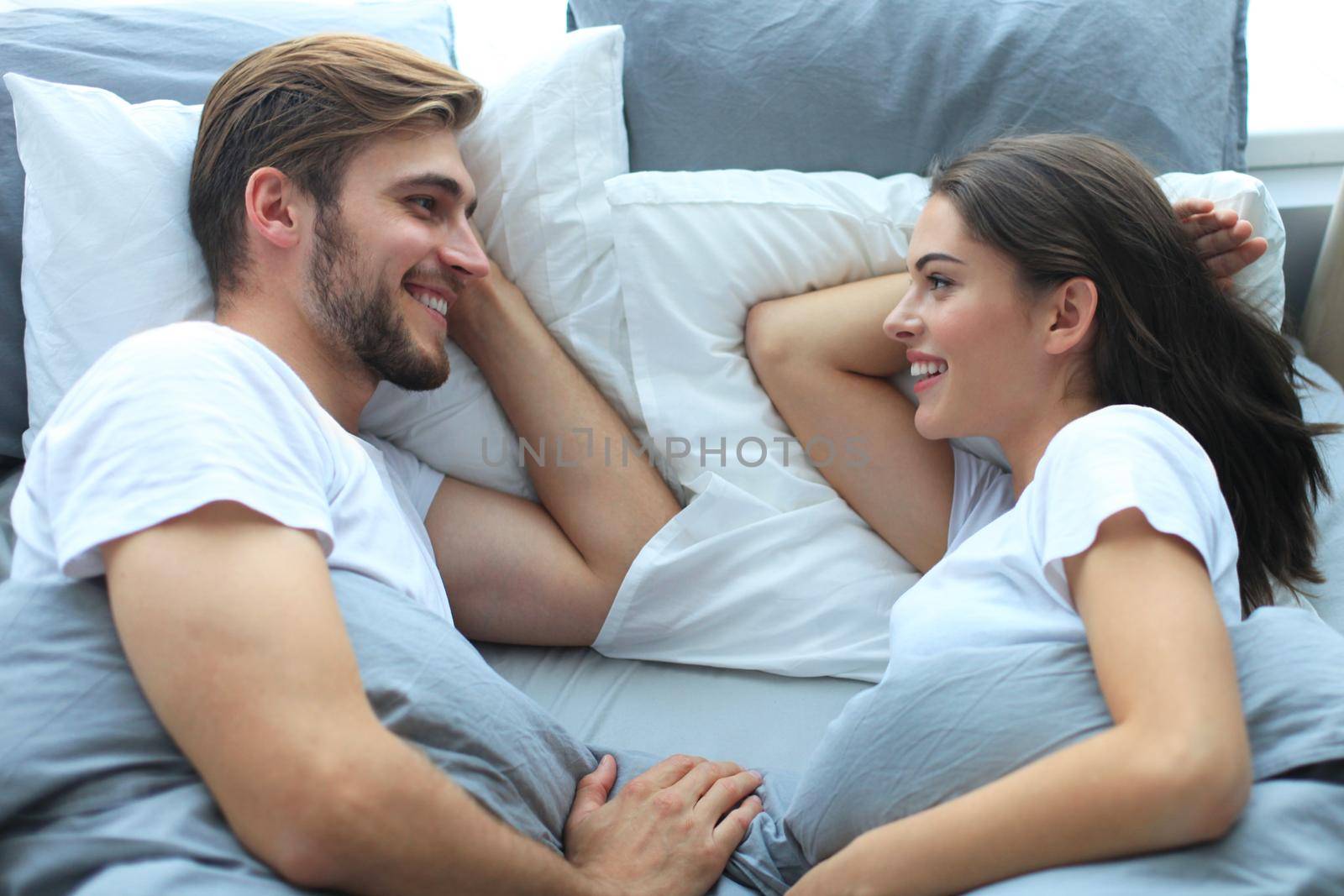 Cheerful couple awaking and looking at each other in bed. by tsyhun