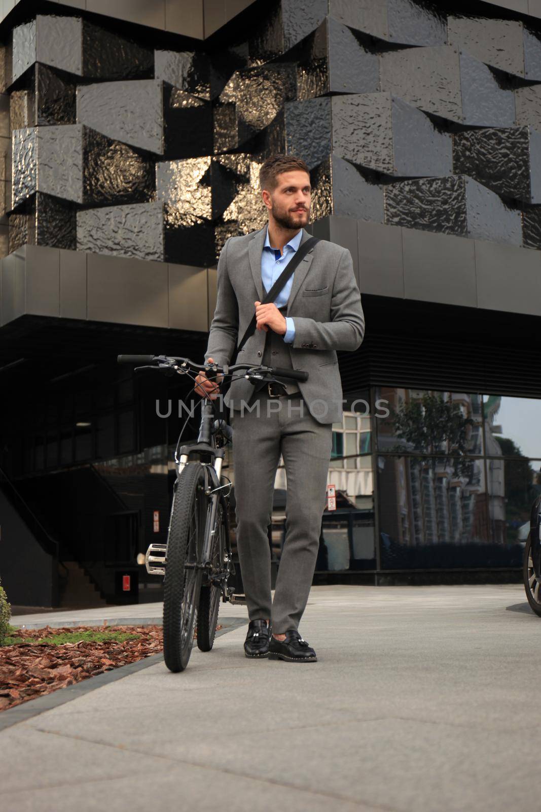Confident young businessman walking with bicycle on the street in town. by tsyhun