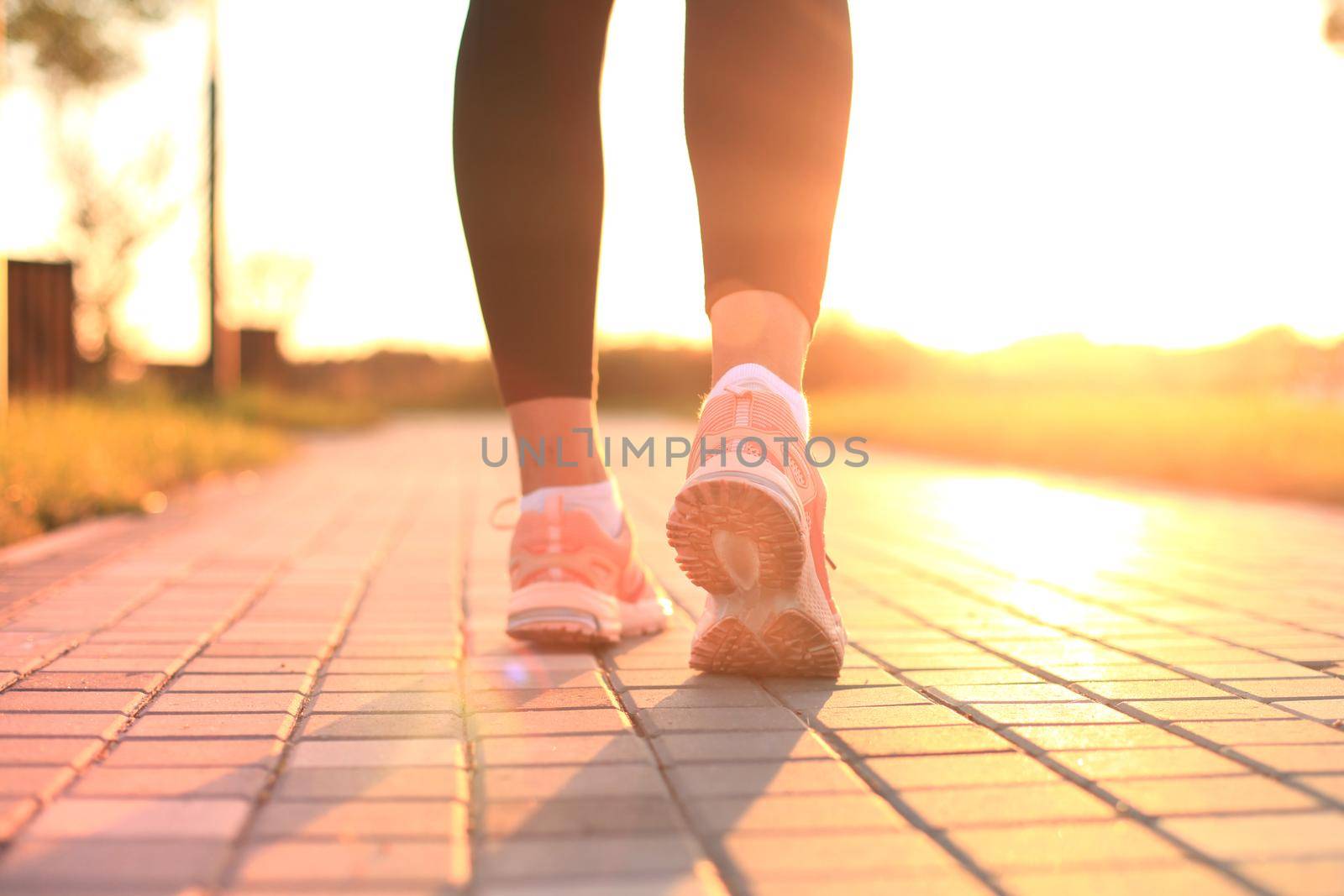 Runner feet running on road closeup on shoe, outdoor at sunset or sunrise in city