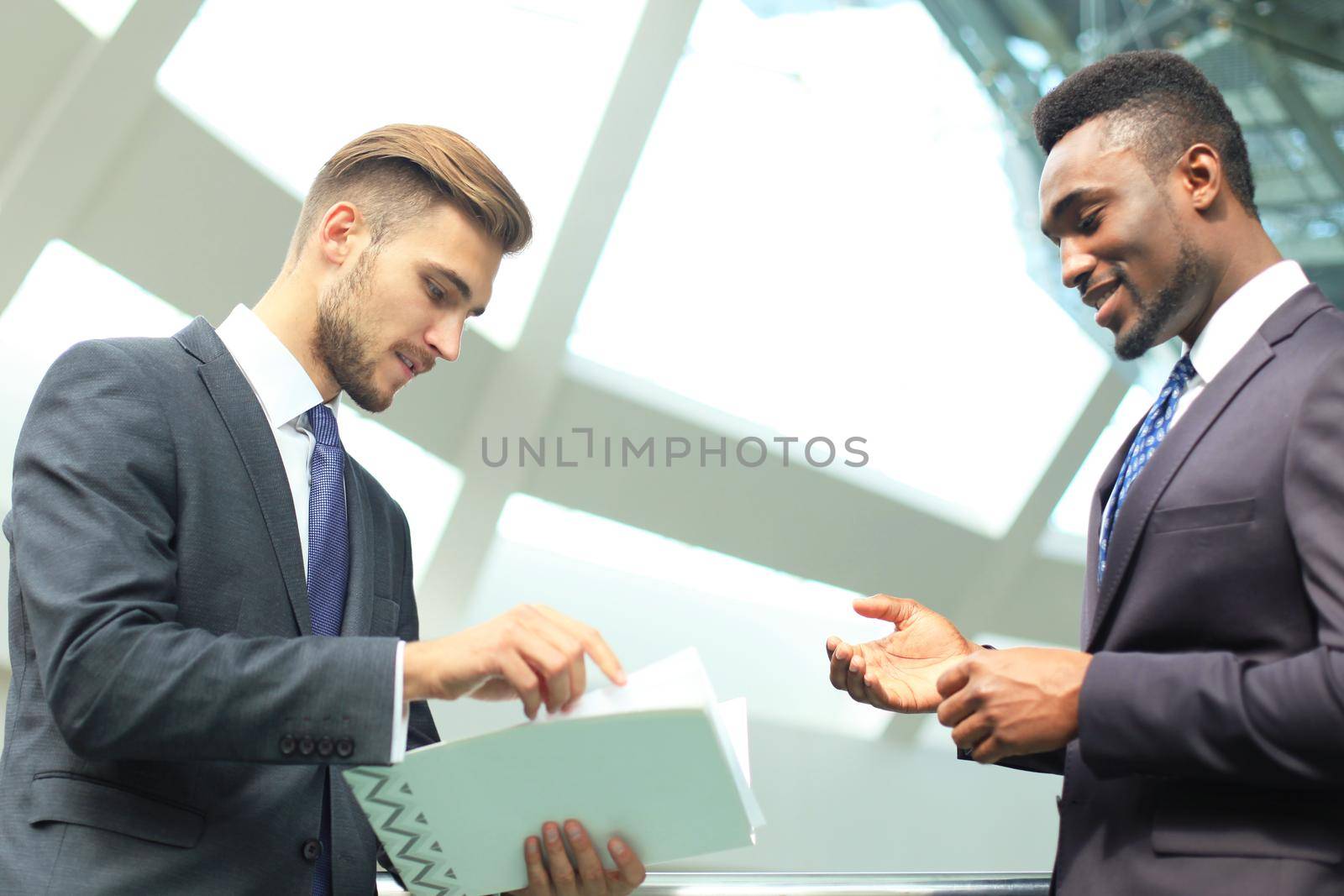 Two multinational young businessmen discussing business at meeting in office.