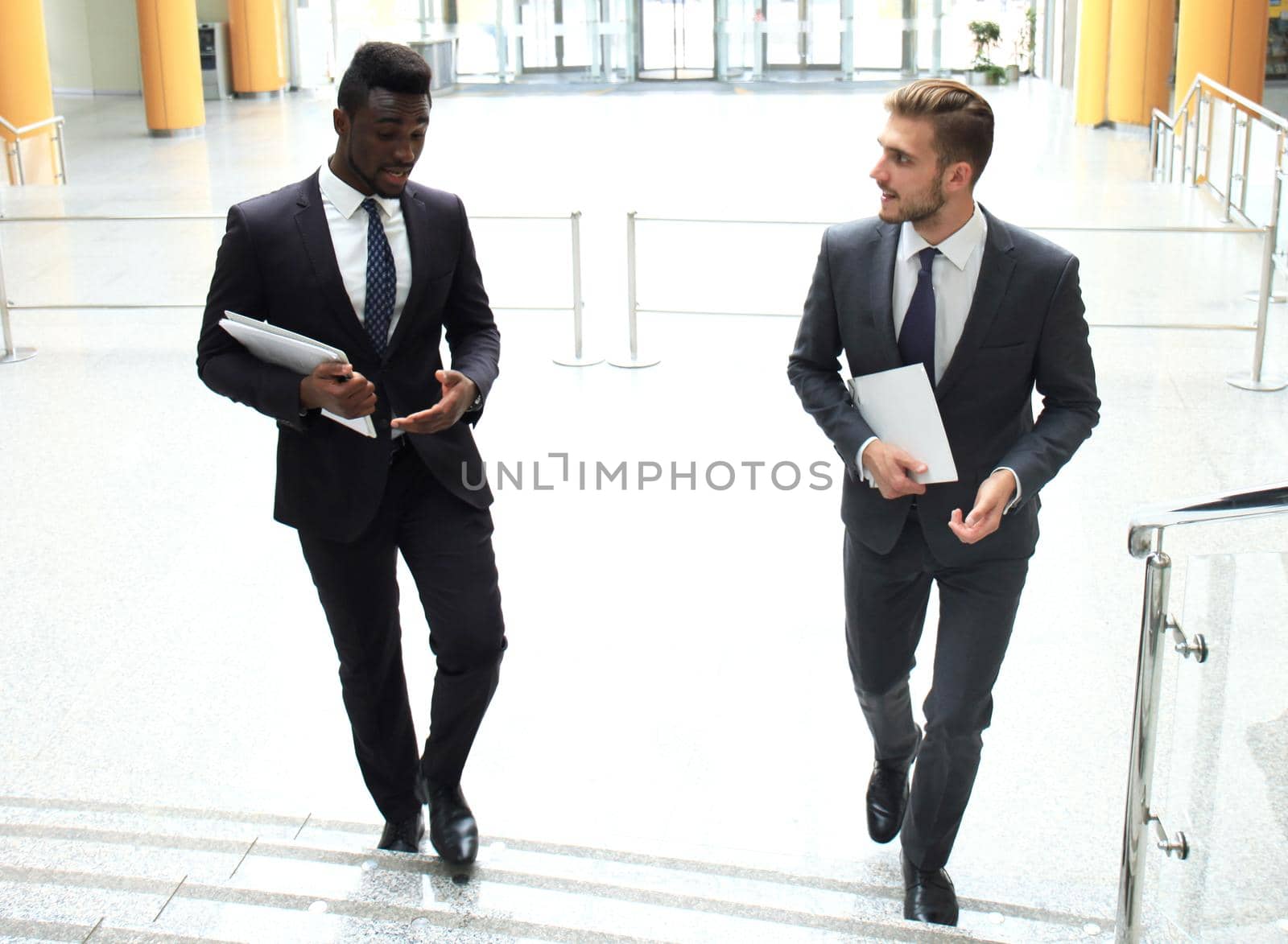 Two multinational young businessmen talking while stairs in modern office building. by tsyhun