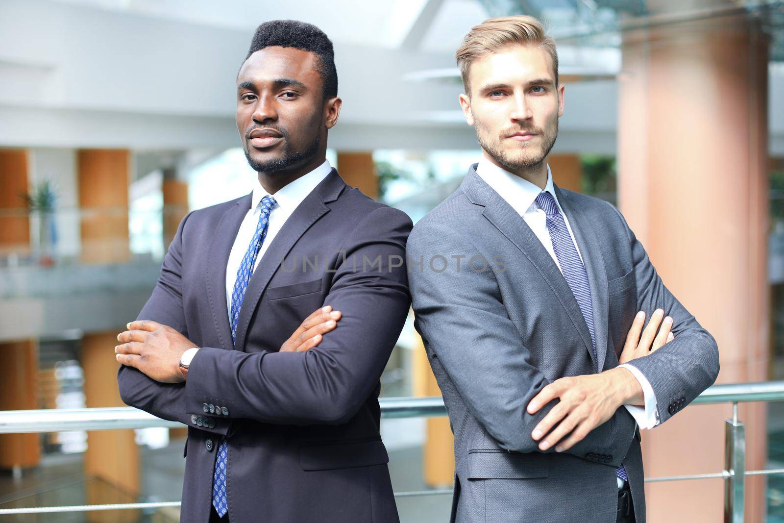African american and caucasian business partners standing back to back together and looking in camera, in office. by tsyhun