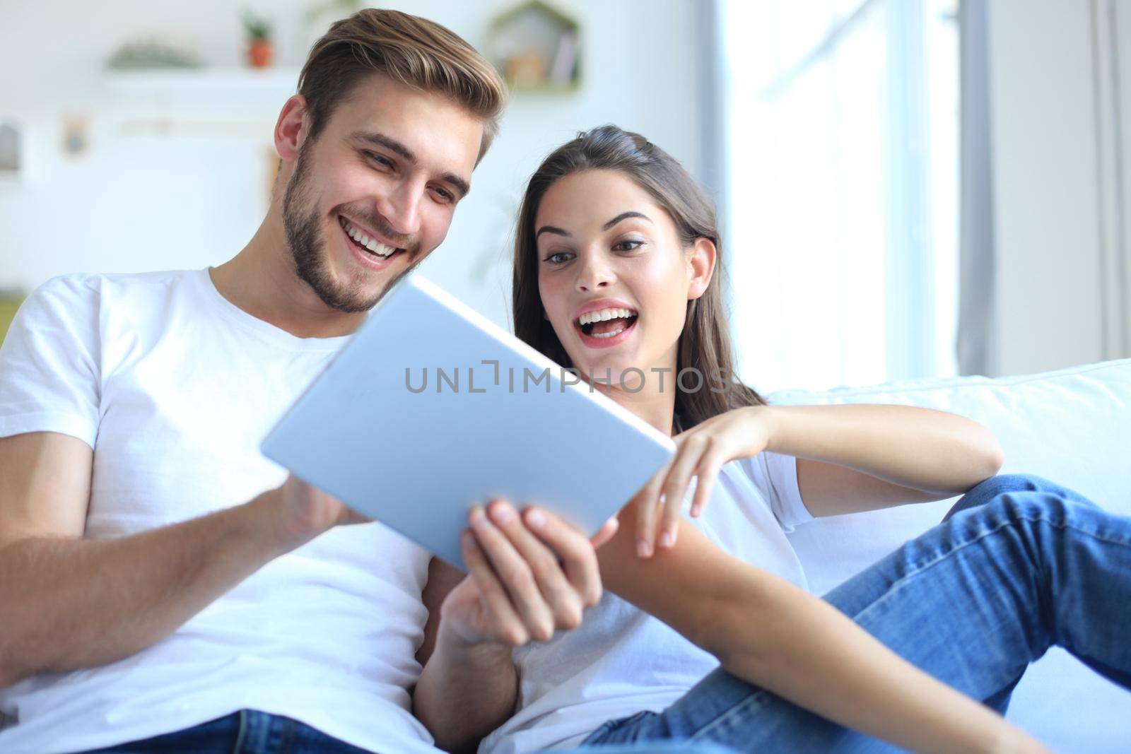 Young couple watching media content online in a tablet sitting on a sofa in the living room.