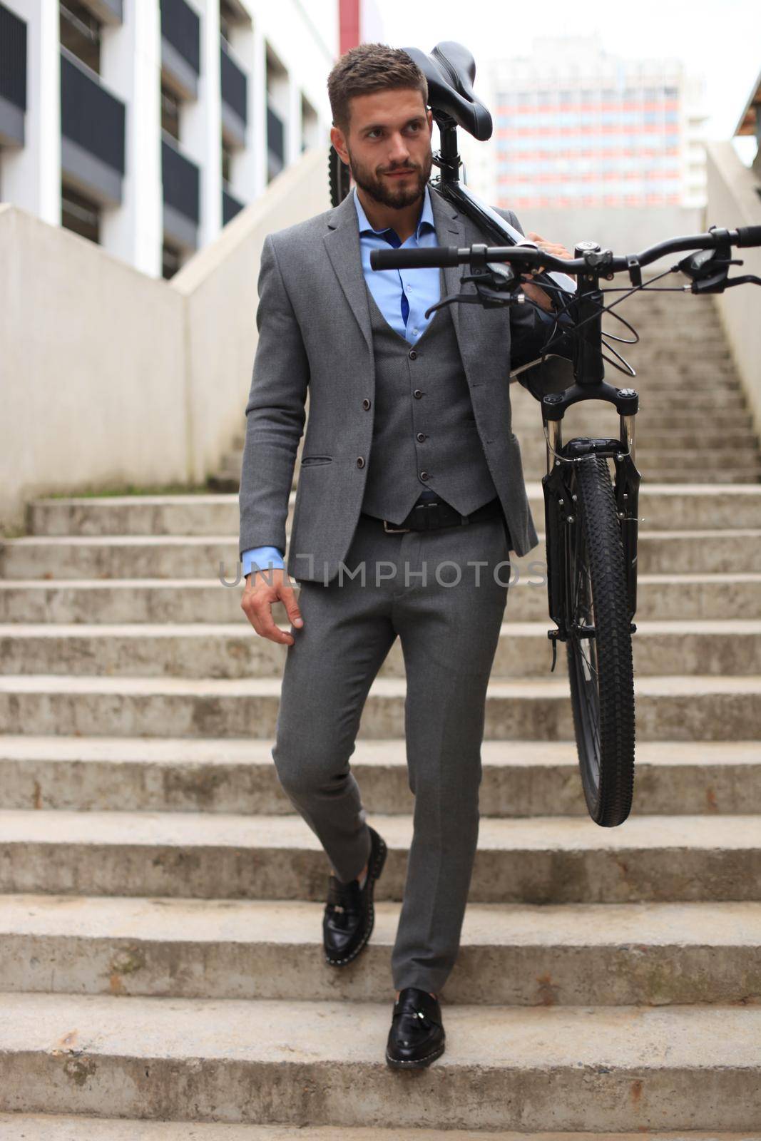 Confident young businessman carrying his bicycle while walking outdoors.