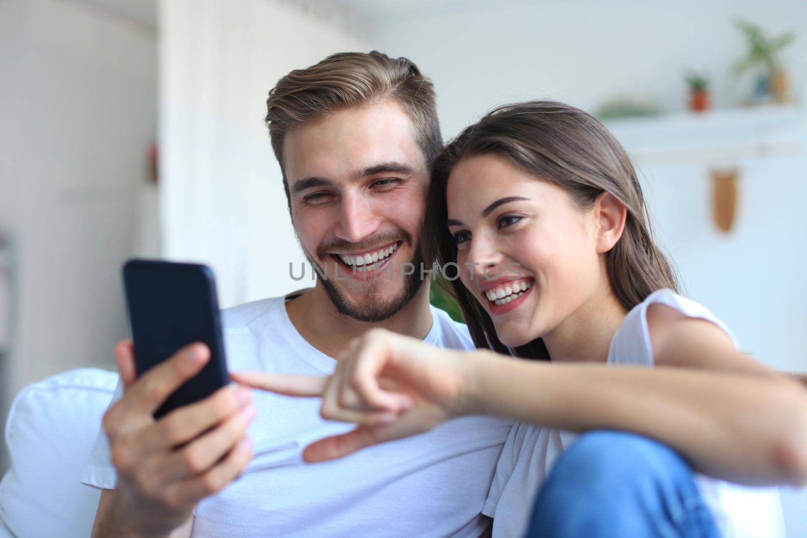 Young couple watching online content in a smart phone sitting on a sofa at home in the living room. by tsyhun