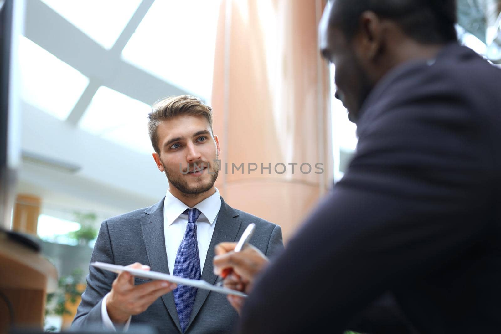 Two multinational young businessmen in suit in the office sign the contract. by tsyhun