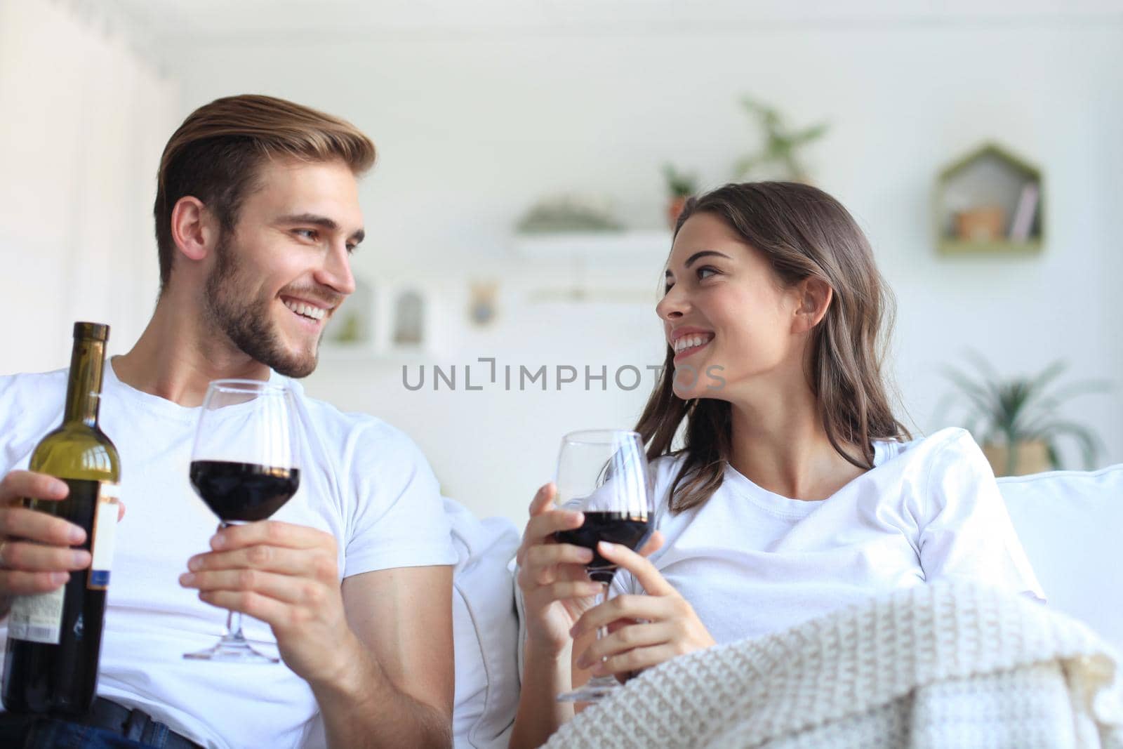 Young loving couple drinking a glass of red wine in their living room. by tsyhun