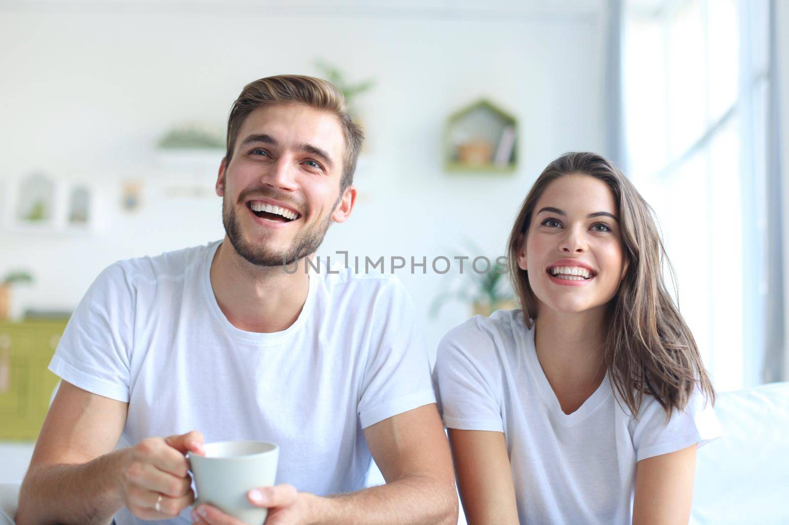 Young loving couple on sofa at home watching tv and laughing. by tsyhun
