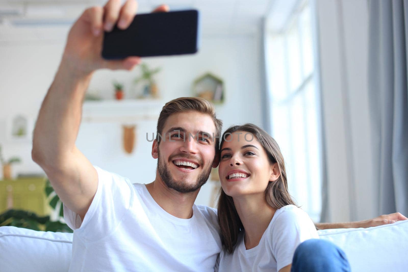 Young couple taking a selfie on couch at home in the living room. by tsyhun