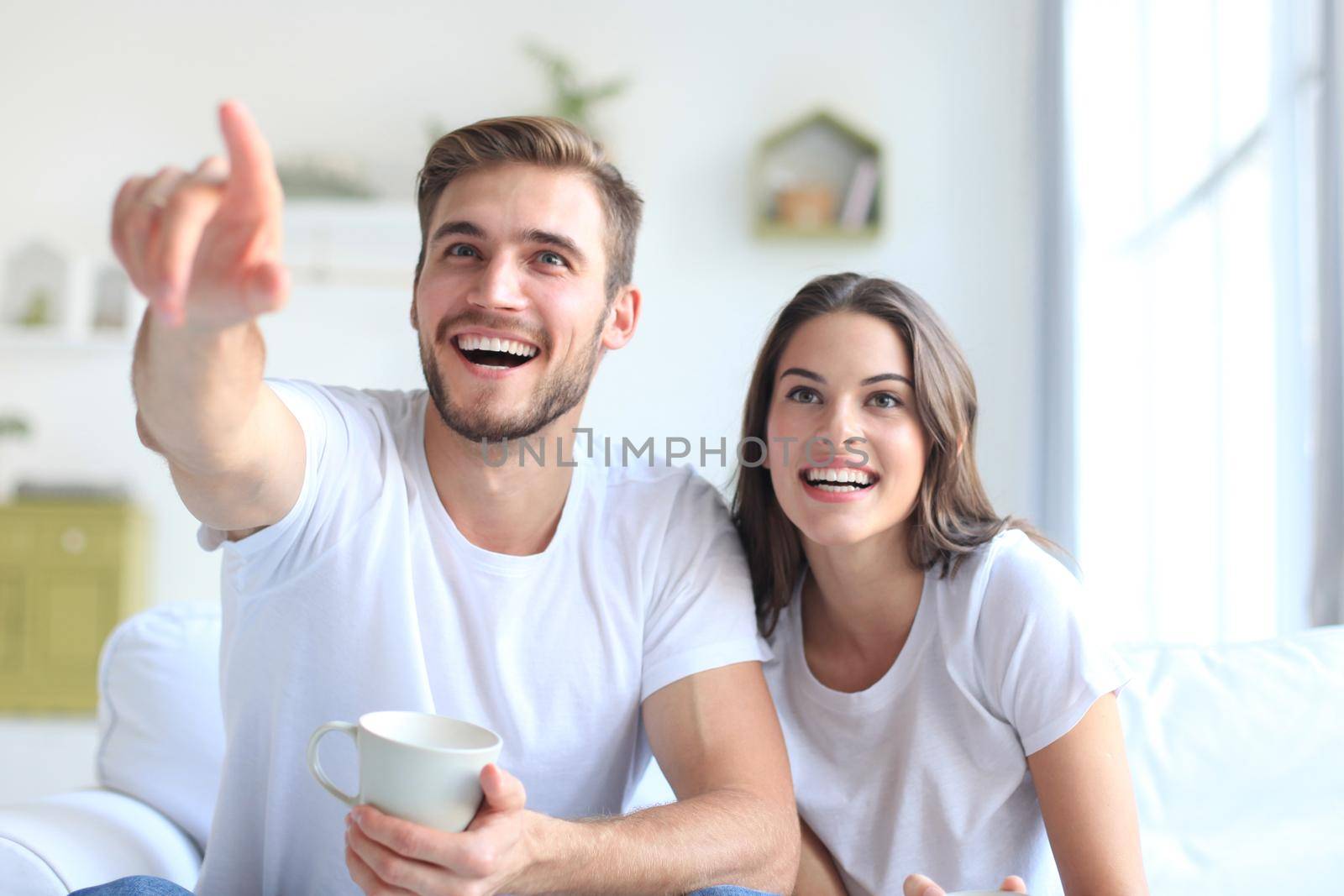 Young loving couple on sofa at home watching tv and laughing.