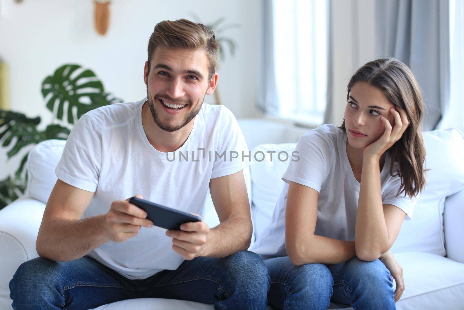 Man playing video games while his girlfriend is getting mad at him in their living room. by tsyhun
