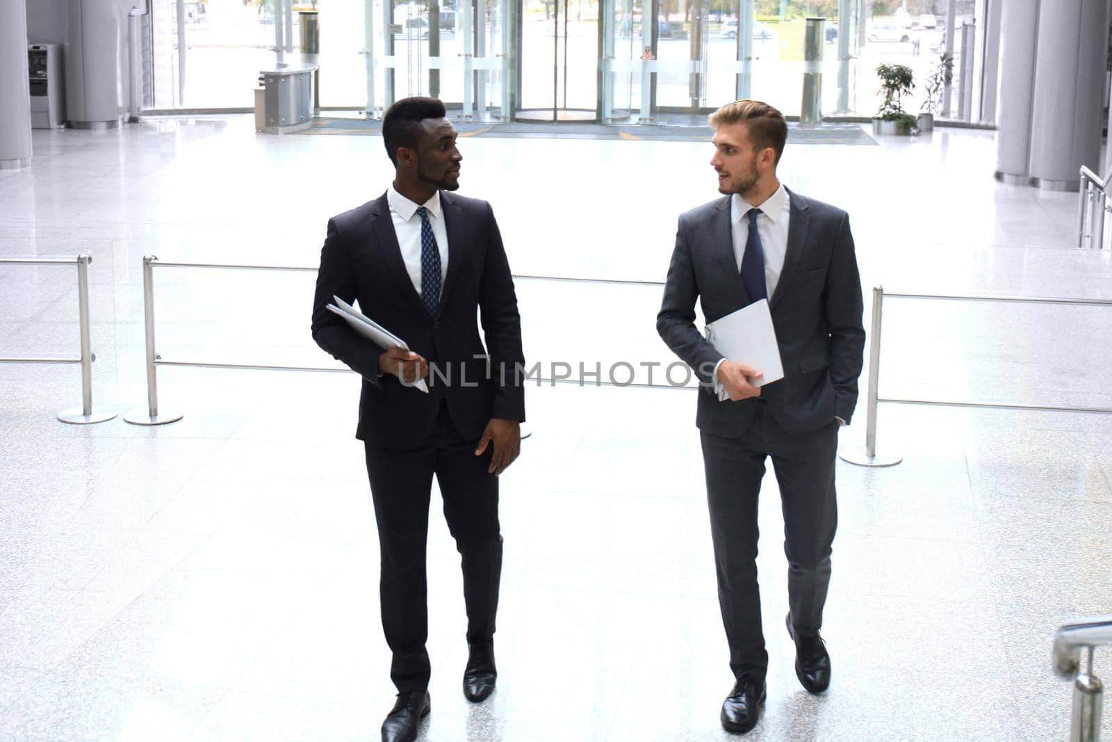 Two multinational young businessmen talking while stairs in modern office building.