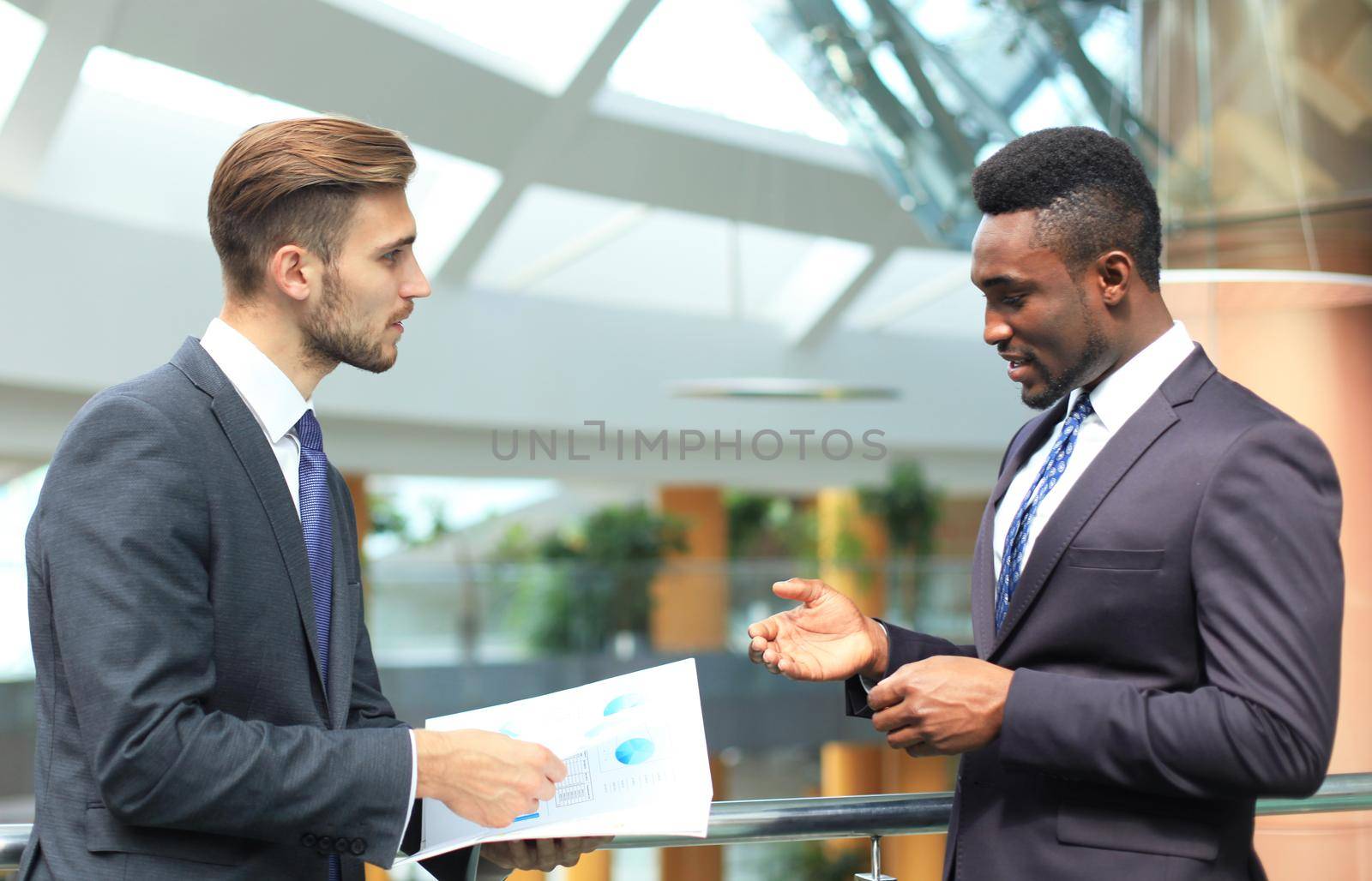 Two multinational young businessmen discussing business at meeting in office.