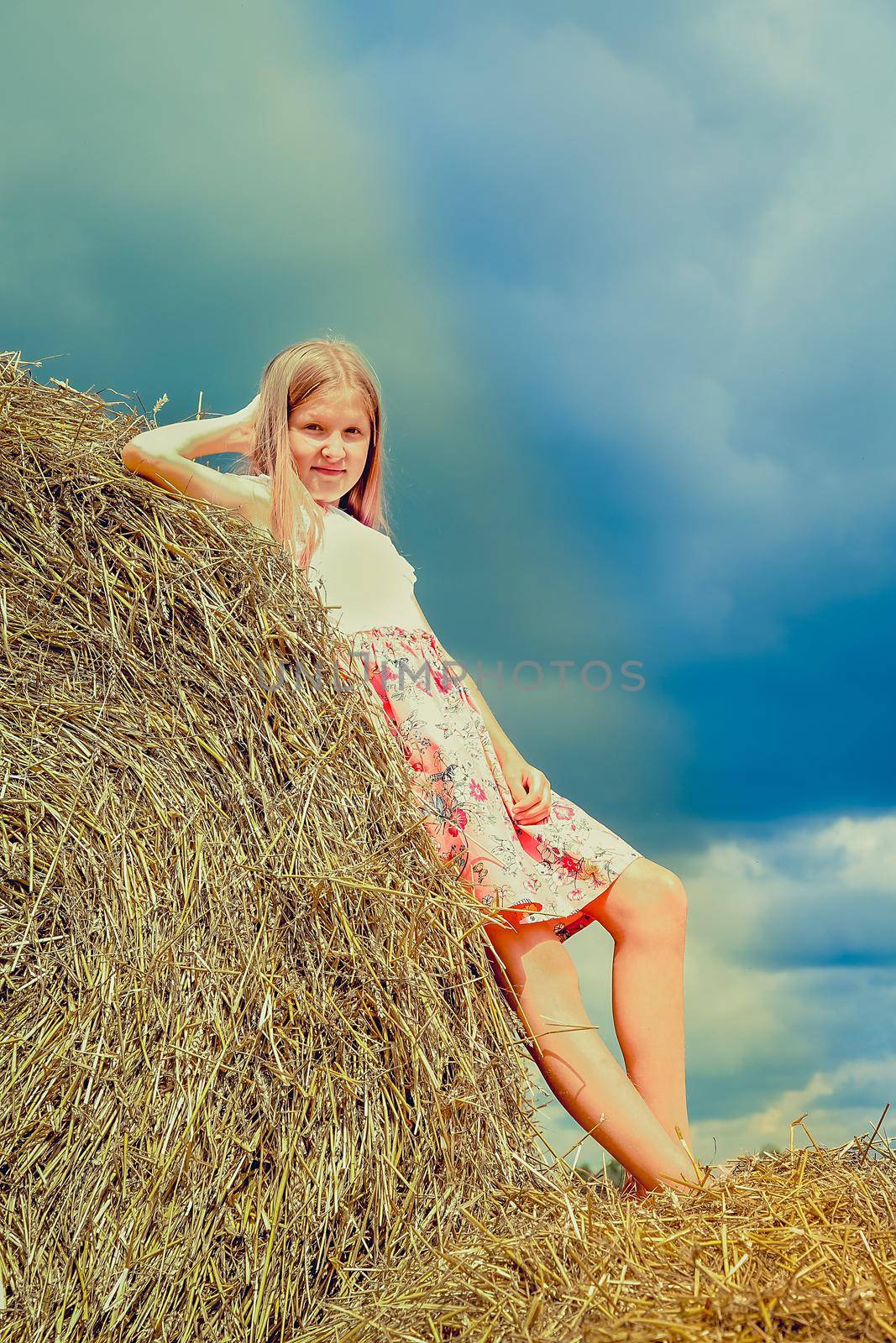 A girl with long flowing hair in a pink dress climbed on large bales of straw
